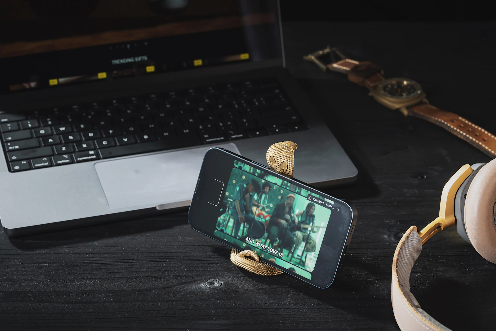Smartphone on a stand beside headphones and a laptop