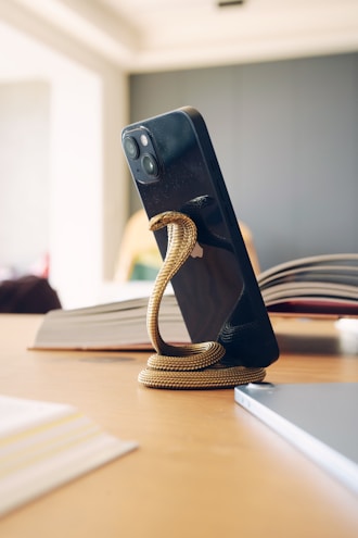 A sleek 3D-printed phone stand holding a smartphone on a wooden desk.