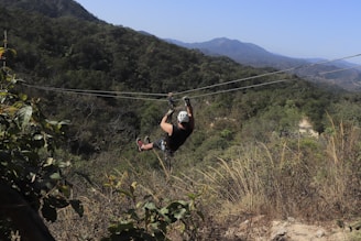 A zip-line glider soaring through the sky over a tropical landscape.
