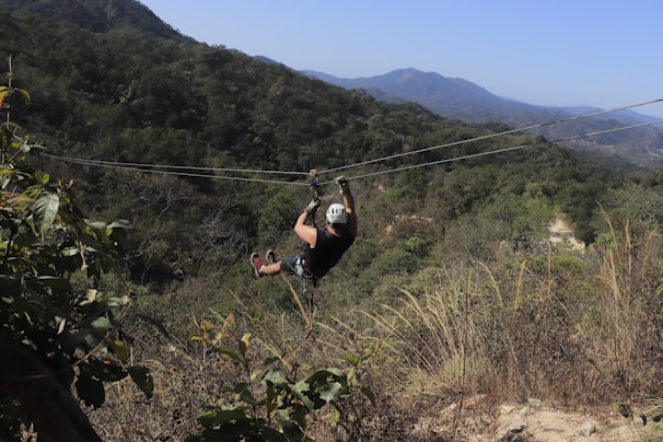 A zip-line glider soaring through the sky over a tropical landscape.