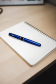 Close-up of a notebook and pen on a sleek desk with subtle blue gradient background.