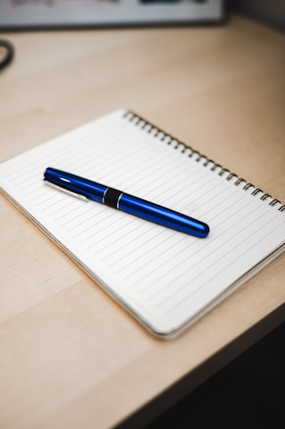 Close-up of a notebook open with a pen placed neatly beside it on a wooden desk.