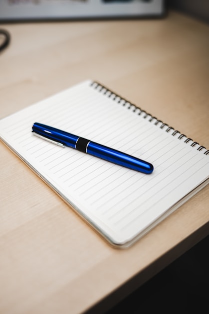 Ballpoint pen resting diagonally across an open notebook on a minimal desk
