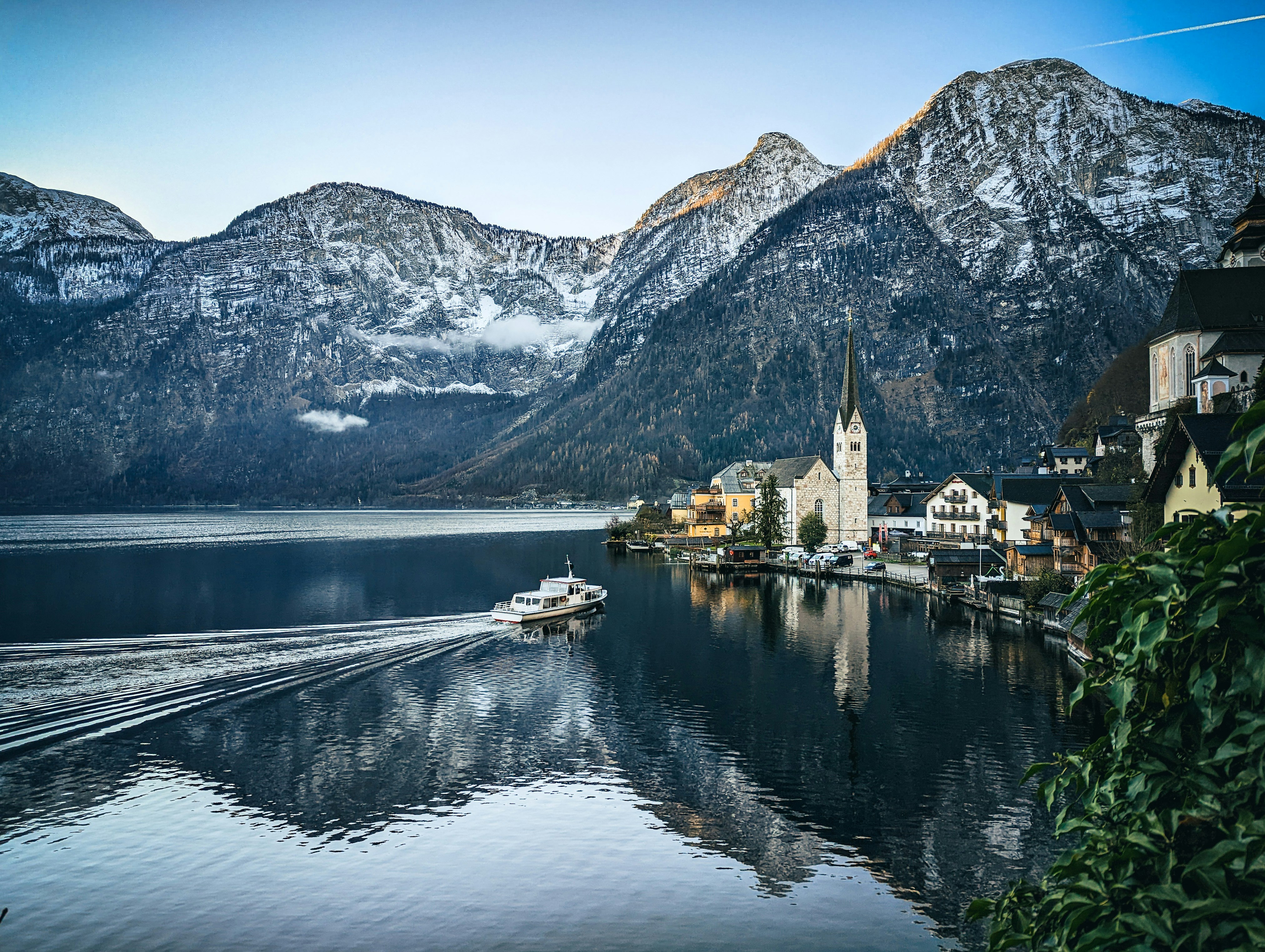 a boat traveling down a river next to a mountain range, Beautiful morning in Hallstadt