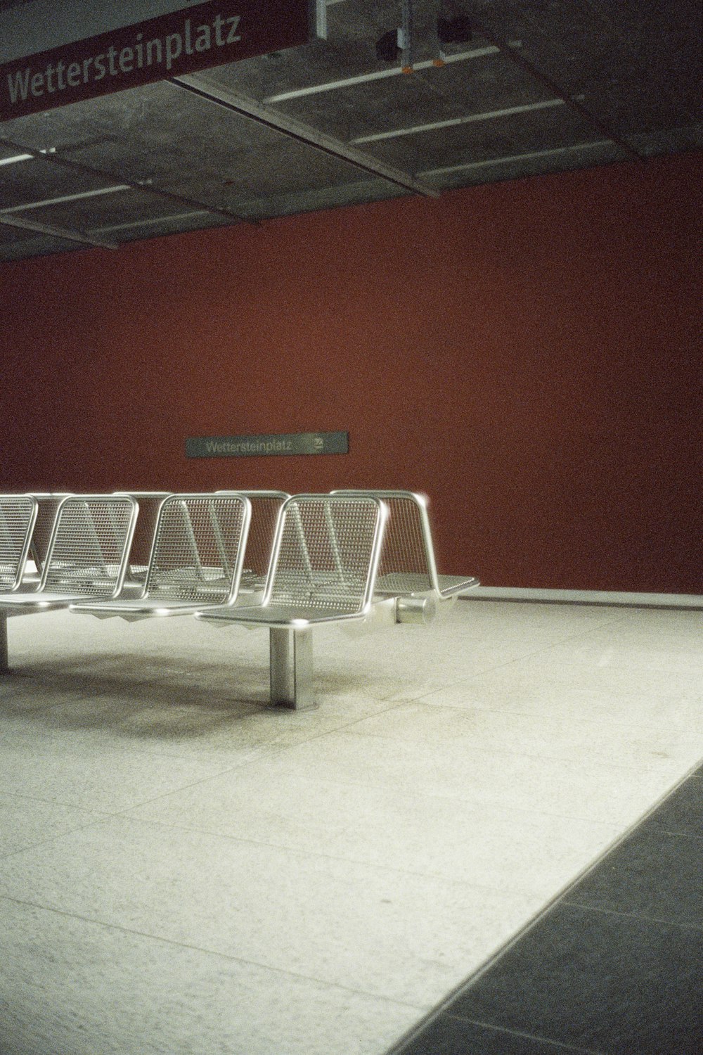 a row of metal benches sitting next to a red wall