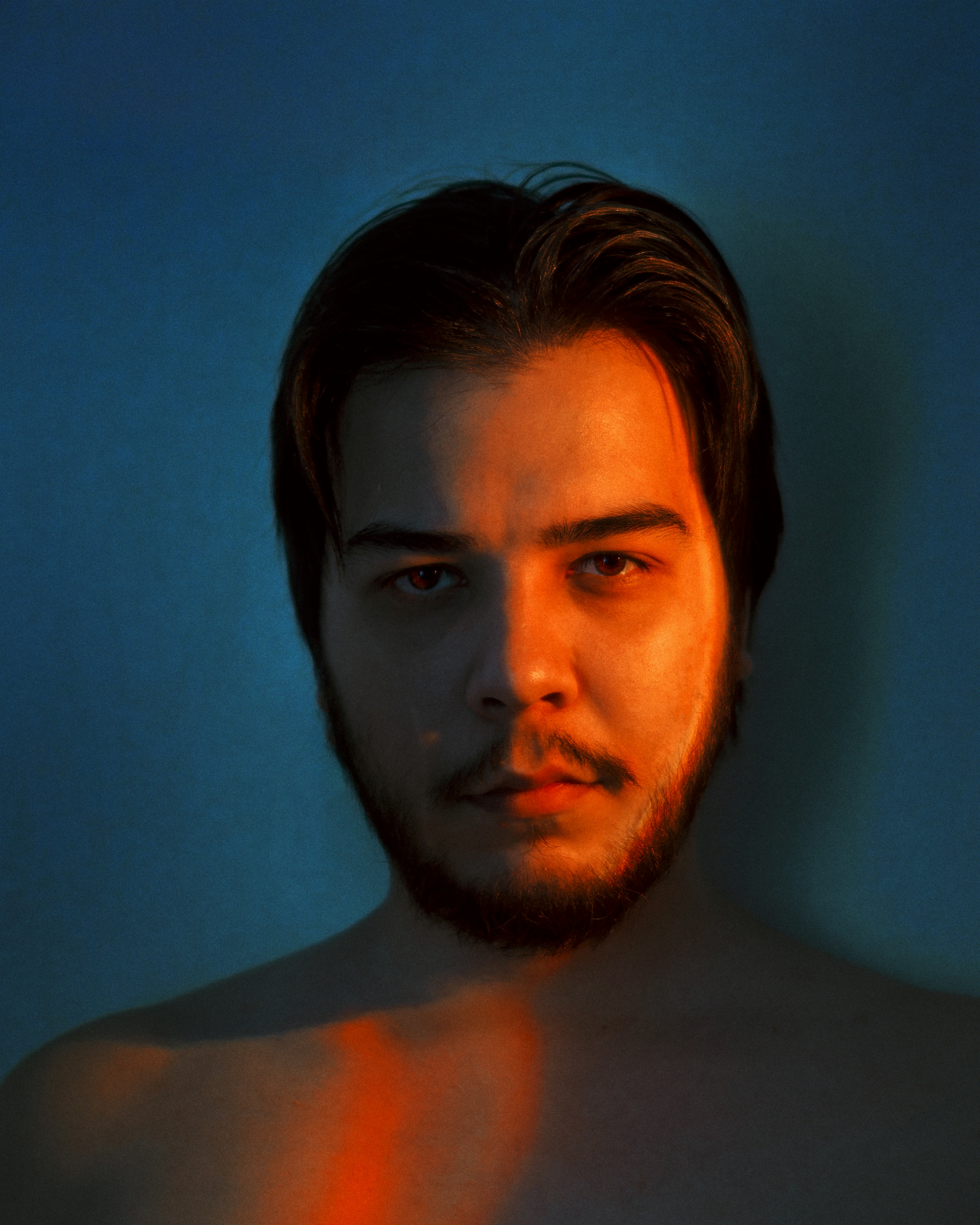 A warm portrait of a muscular, handsome nonbinary adult services provider against a rich brown backdrop.
