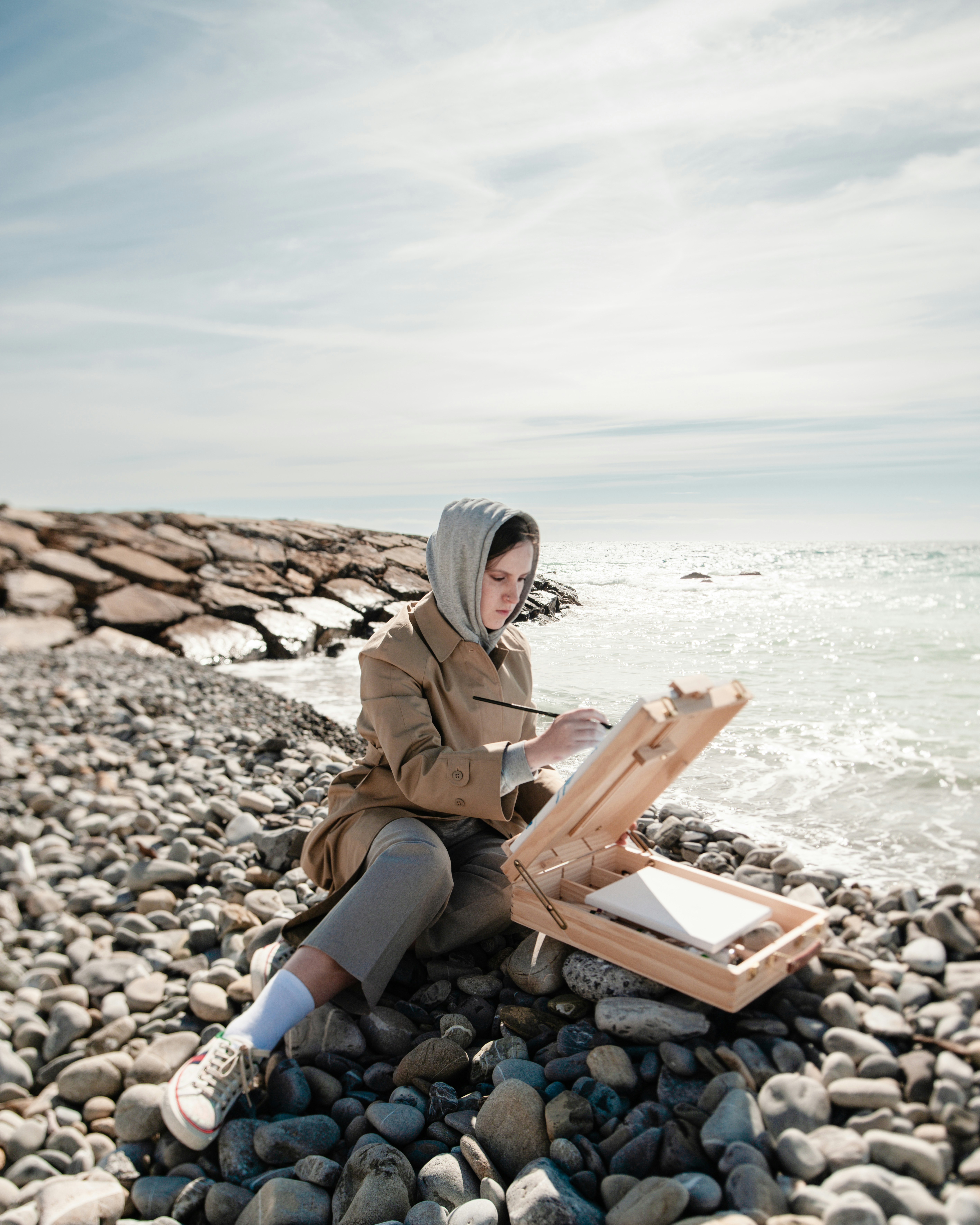a woman sitting on a rocky beach next to the ocean