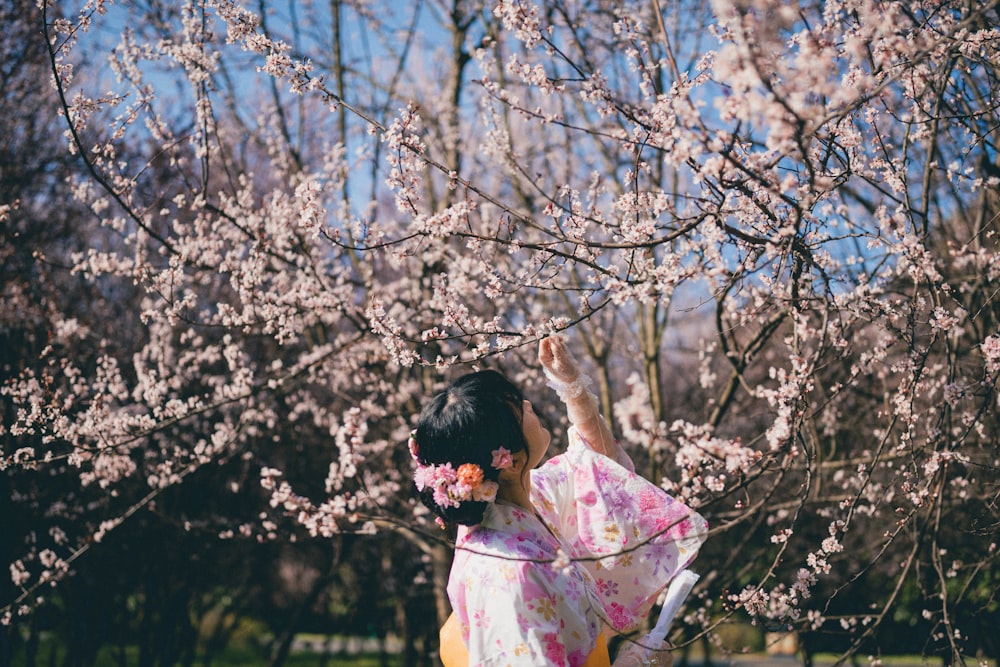 a woman in a kimono reaching up to a cherry blossom tree