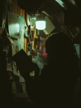A shadowy figure reading under turquoise light, surrounded by stacks of confidential files.