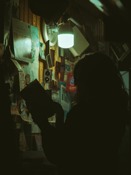 A shadowy figure reading under turquoise light, surrounded by stacks of confidential files.