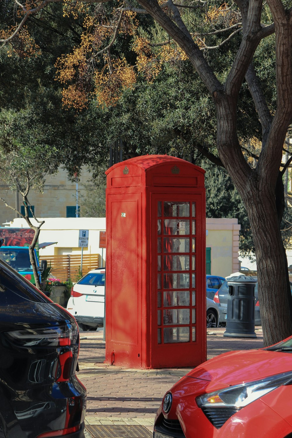 a red phone booth sitting next to a tree