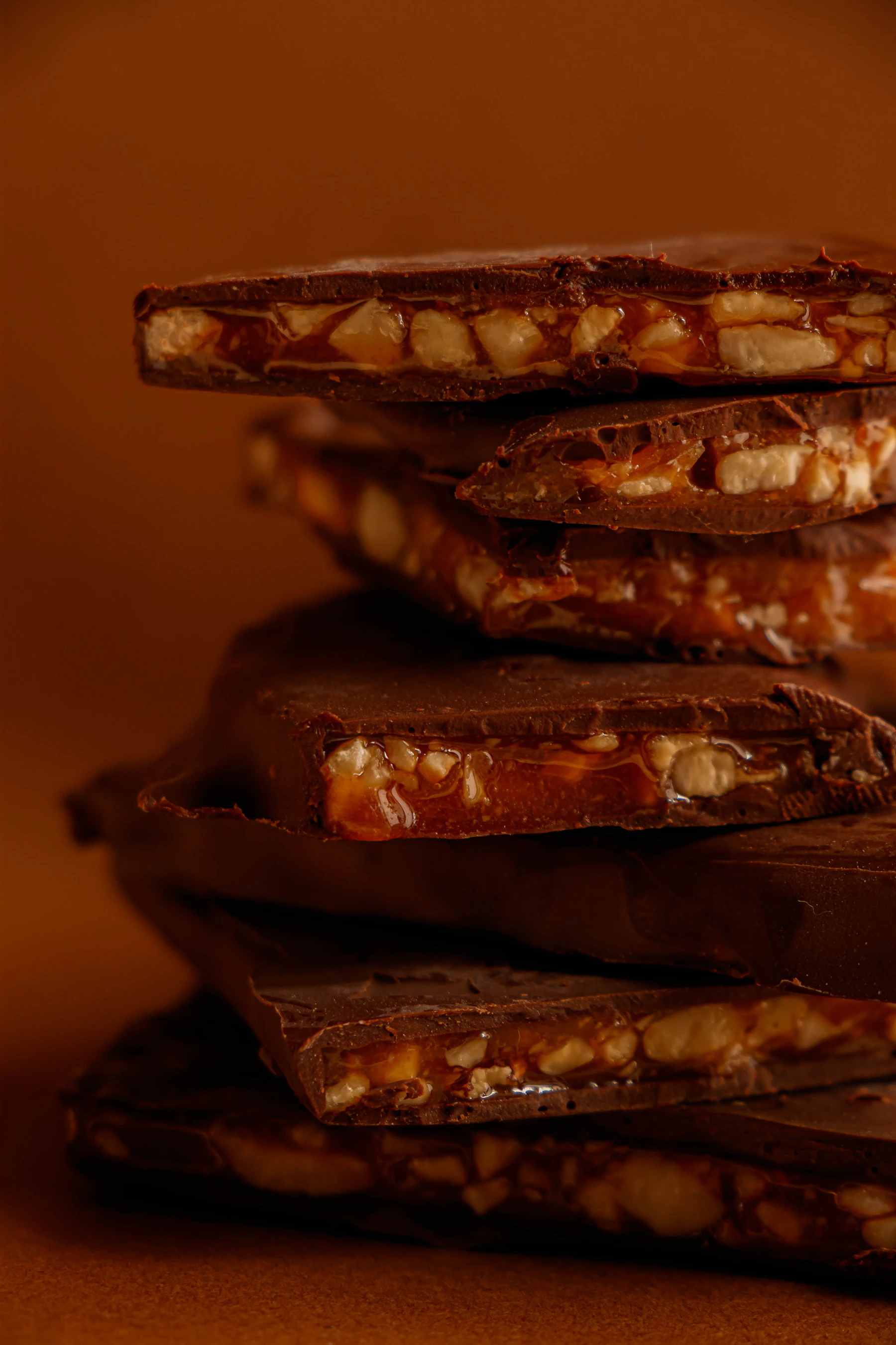 A stack of chocolate-topped toffee pieces, the nut and caramel layer showing at the broken edges