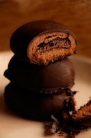A delectable stack of round chocolate-covered cookies with one partially bitten, revealing a rich inner layer of chocolate filling. Crumbs are scattered around the base, adding a rustic feel.