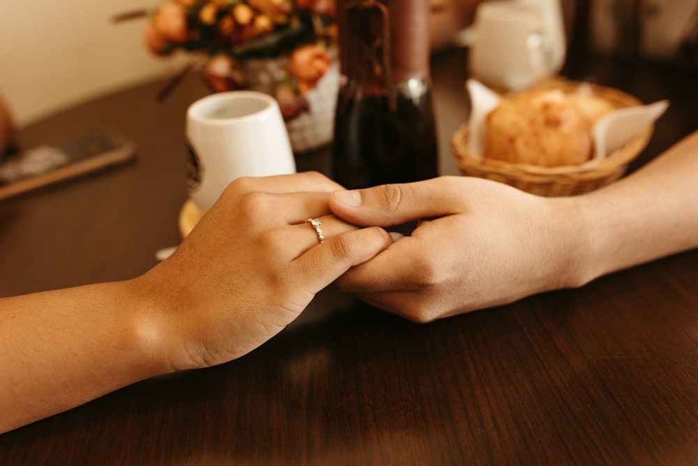 two people holding hands over a table with a basket of bread