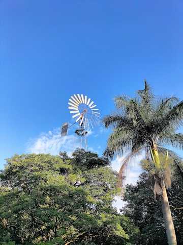 Windmill turbines turning gracefully against a clear blue sky in an industrial area.