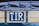 A close-up view of a wooden and metal structure with a sign that has the letters 'T.I.R' on it. The structure is part of a covered vehicle with a tarpaulin attached using metal hooks and ropes.