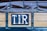 A close-up view of a wooden and metal structure with a sign that has the letters 'T.I.R' on it. The structure is part of a covered vehicle with a tarpaulin attached using metal hooks and ropes.