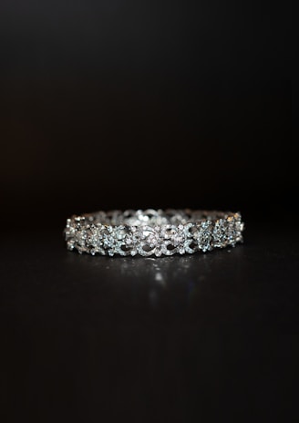 A beautifully crafted diamond bracelet lies against a dark background. The intricate design features multiple small diamonds arranged in a symmetrical pattern, enhancing its elegance and sparkle.