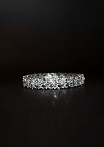 A beautifully crafted diamond bracelet lies against a dark background. The intricate design features multiple small diamonds arranged in a symmetrical pattern, enhancing its elegance and sparkle.