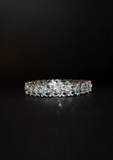 A beautifully crafted diamond bracelet lies against a dark background. The intricate design features multiple small diamonds arranged in a symmetrical pattern, enhancing its elegance and sparkle.