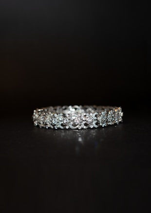 A beautifully crafted diamond bracelet lies against a dark background. The intricate design features multiple small diamonds arranged in a symmetrical pattern, enhancing its elegance and sparkle.