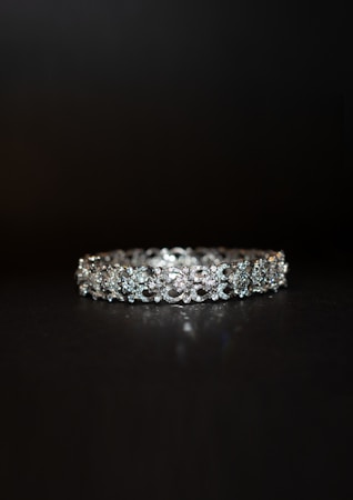 A beautifully crafted diamond bracelet lies against a dark background. The intricate design features multiple small diamonds arranged in a symmetrical pattern, enhancing its elegance and sparkle.