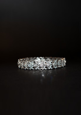 A beautifully crafted diamond bracelet lies against a dark background. The intricate design features multiple small diamonds arranged in a symmetrical pattern, enhancing its elegance and sparkle.