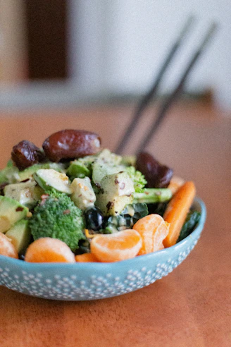 a blue bowl filled with broccoli, carrots and other vegetables