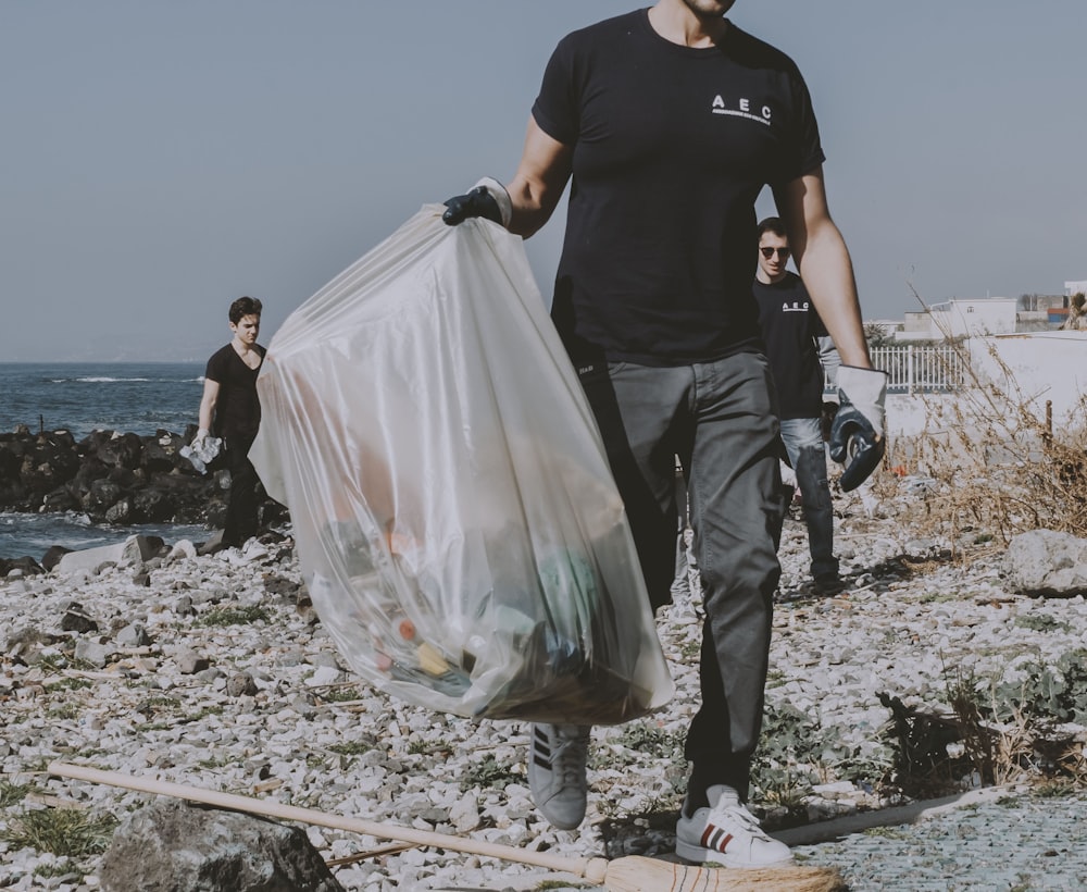 a man walking on a beach carrying a bag of garbage
