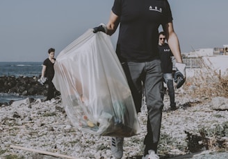 a man walking on a beach carrying a bag of garbage