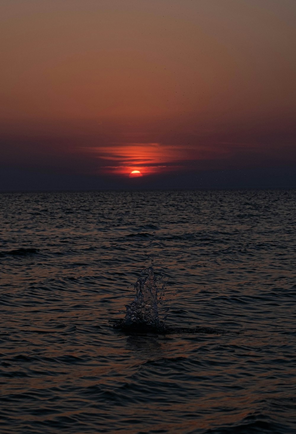 the sun is setting over the ocean with a boat in the water