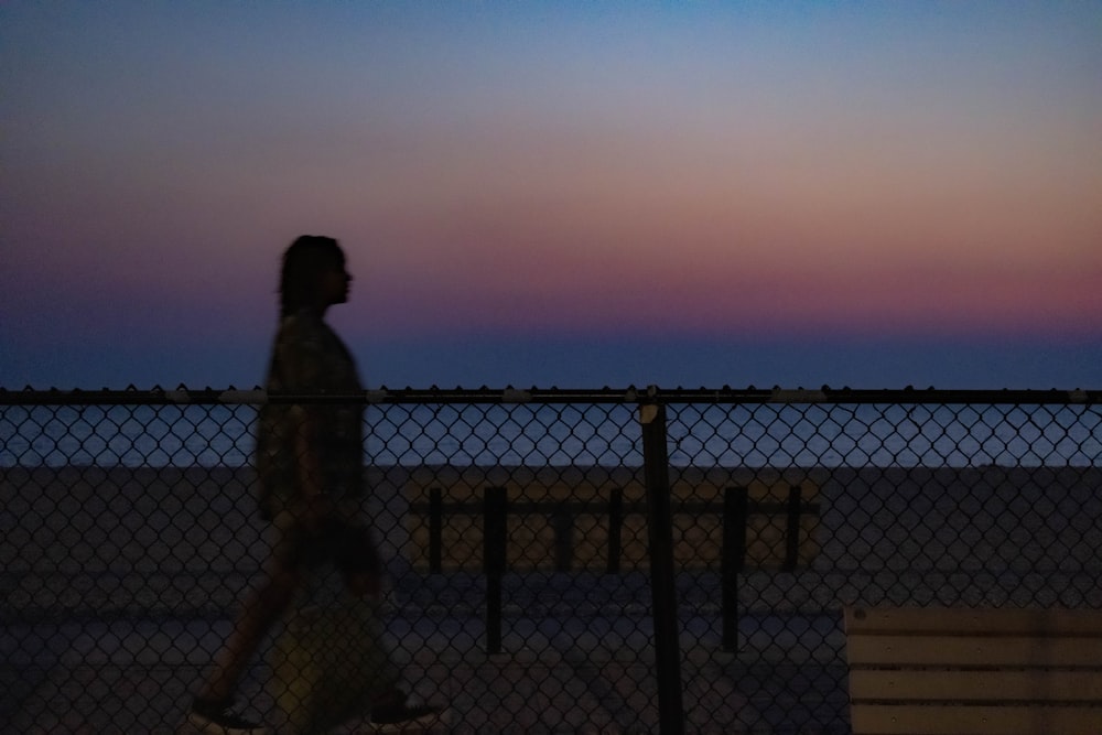 a woman walking past a fence at dusk