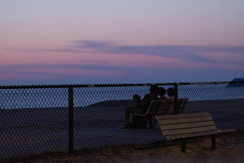 a couple of people sitting on a bench next to a fence