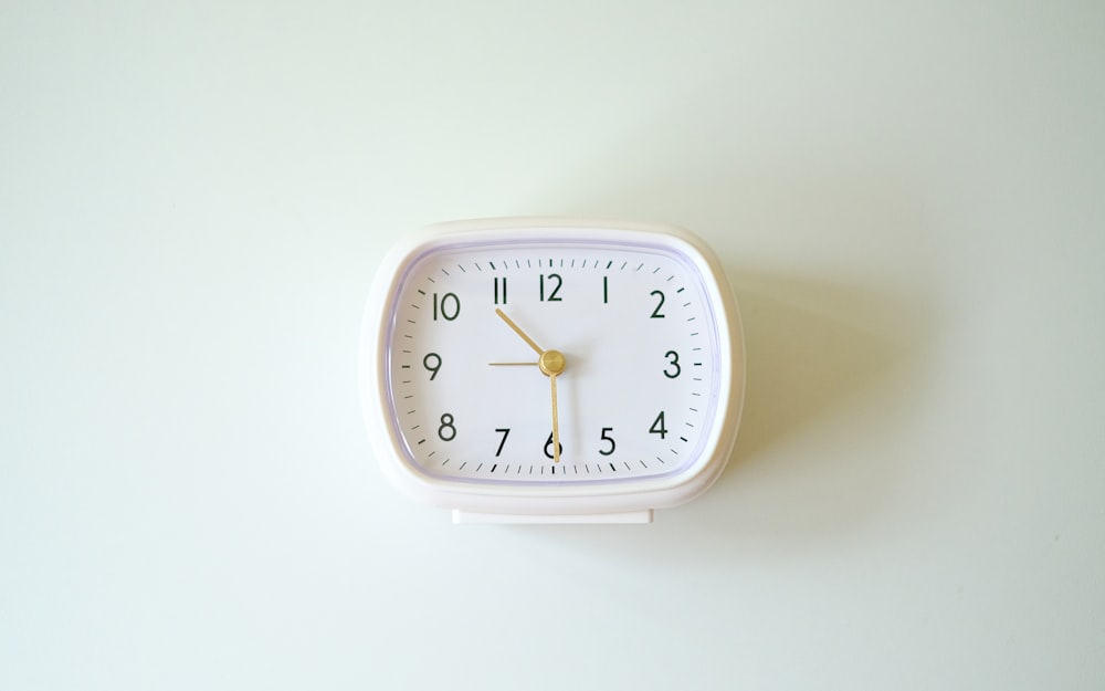 une petite horloge blanche posée au sommet d’un mur blanc