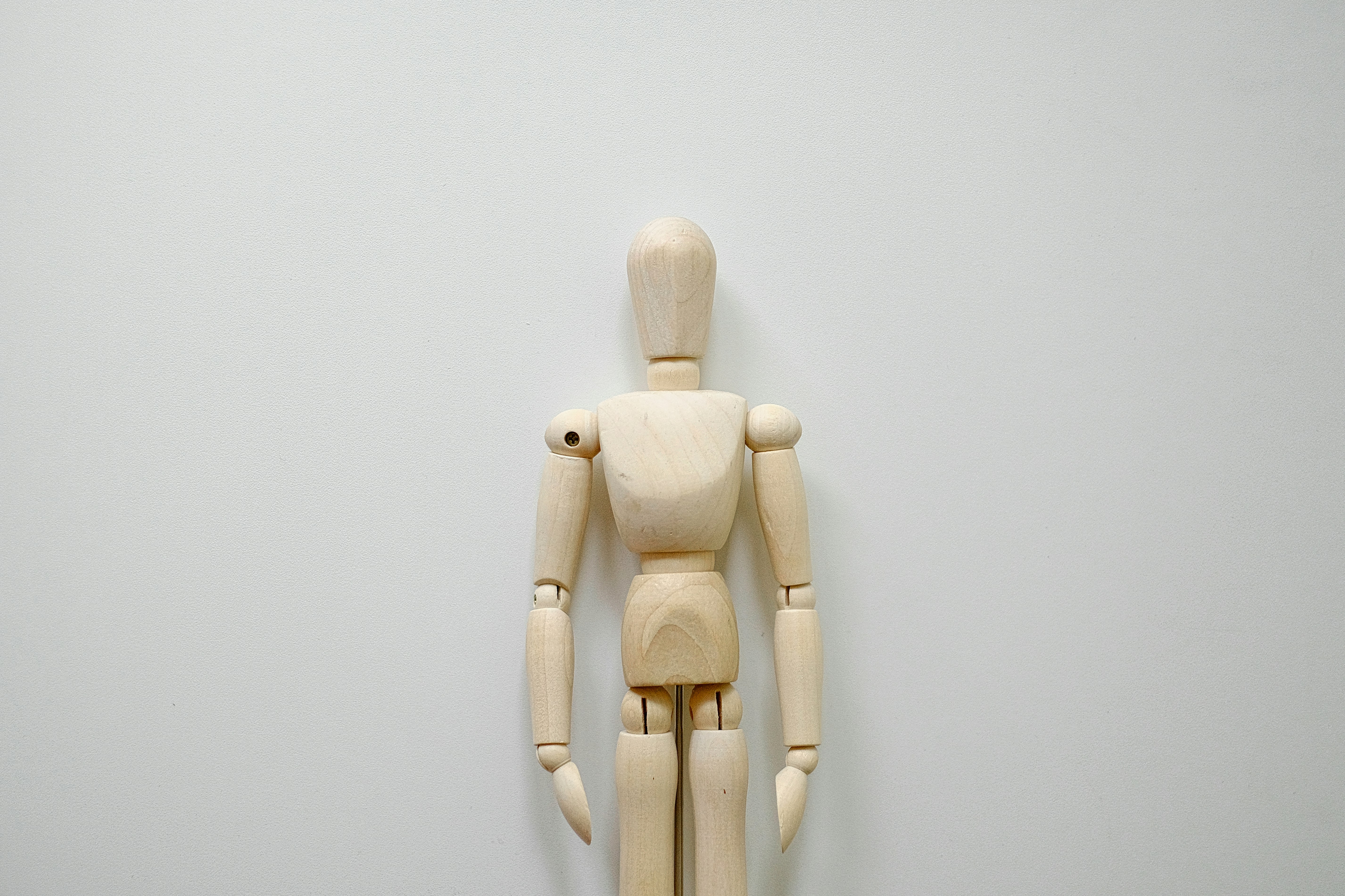 a wooden mannequin standing in front of a white wall