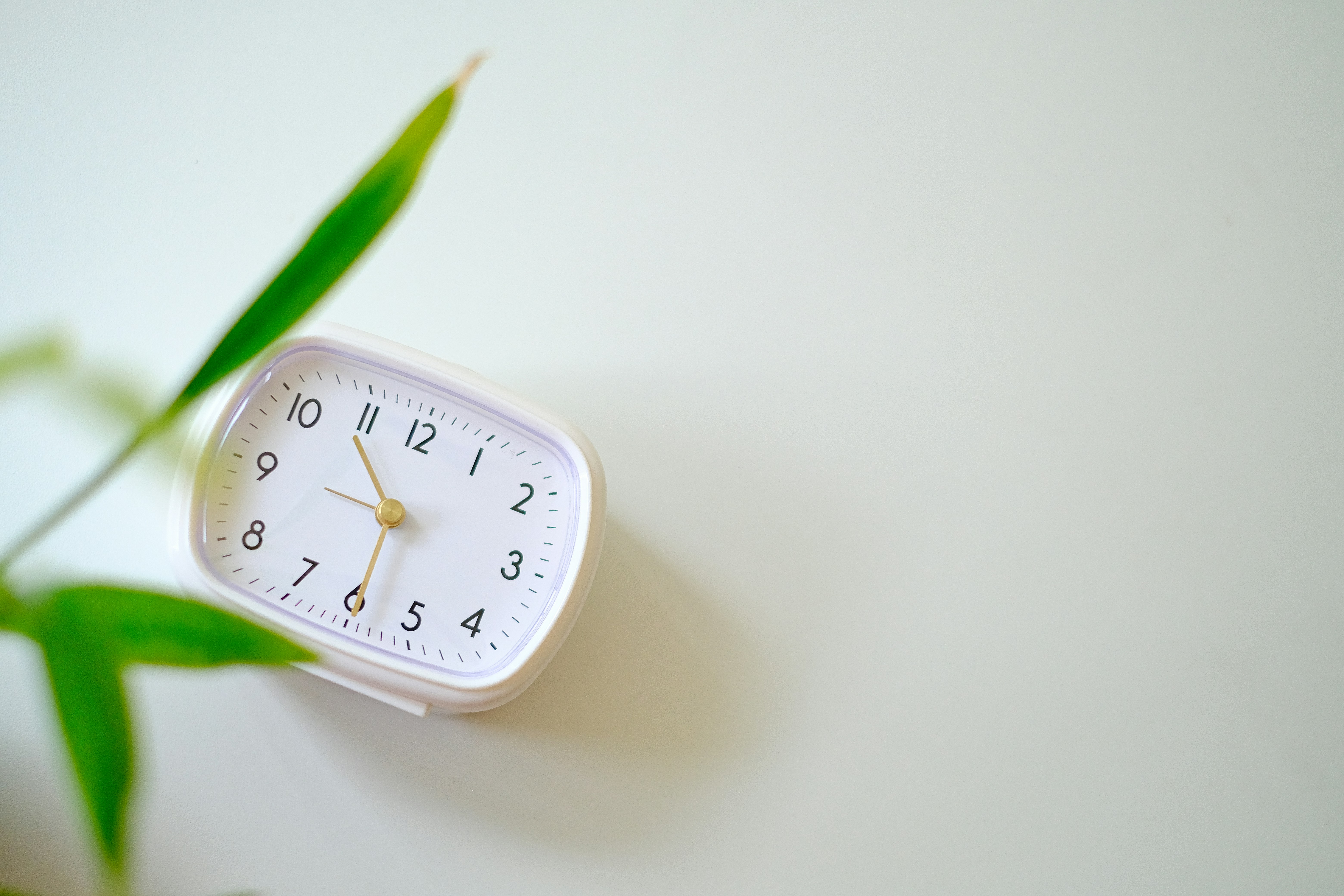 a white clock sitting on top of a table next to a green plant