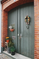 Classic red front door adorned with seasonal wreath, surrounded by flower pots.