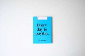 A blue card with the phrase 'Every day is payday.' printed in bold black letters. The card also has a GoDaddy logo at the bottom.