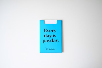 A blue card with the phrase 'Every day is payday.' printed in bold black letters. The card also has a GoDaddy logo at the bottom.