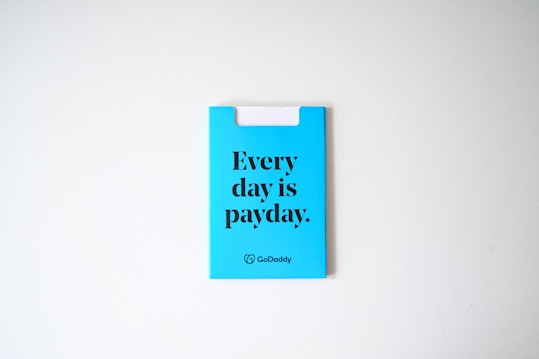 A blue card with the phrase 'Every day is payday.' printed in bold black letters. The card also has a GoDaddy logo at the bottom.