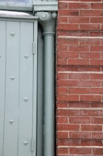 The image displays a section of a building exterior featuring a light green door with embossed diamond patterns beside a vertical downpipe or column. Adjacent to the door is a red brick wall with a clear, straight line of mortar.