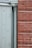 The image displays a section of a building exterior featuring a light green door with embossed diamond patterns beside a vertical downpipe or column. Adjacent to the door is a red brick wall with a clear, straight line of mortar.