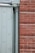 The image displays a section of a building exterior featuring a light green door with embossed diamond patterns beside a vertical downpipe or column. Adjacent to the door is a red brick wall with a clear, straight line of mortar.