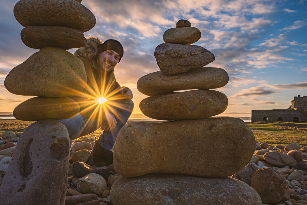 a woman sitting on a pile of rocks with the sun shining behind her