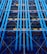 A facade with prominent blue industrial pipes running vertically, intersected by smaller pipes and beams. Various structural elements like scaffolding and platforms are present, along with a mix of colors including yellows and greens.