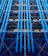 A facade with prominent blue industrial pipes running vertically, intersected by smaller pipes and beams. Various structural elements like scaffolding and platforms are present, along with a mix of colors including yellows and greens.