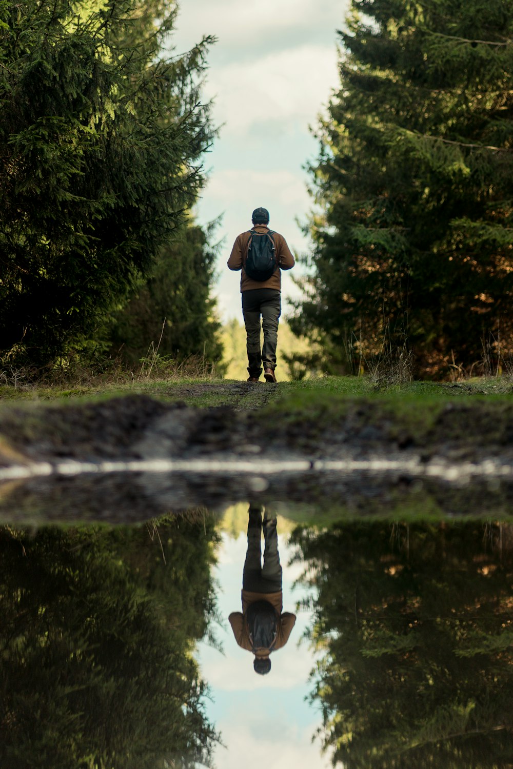 a man walking down a dirt road next to a forest