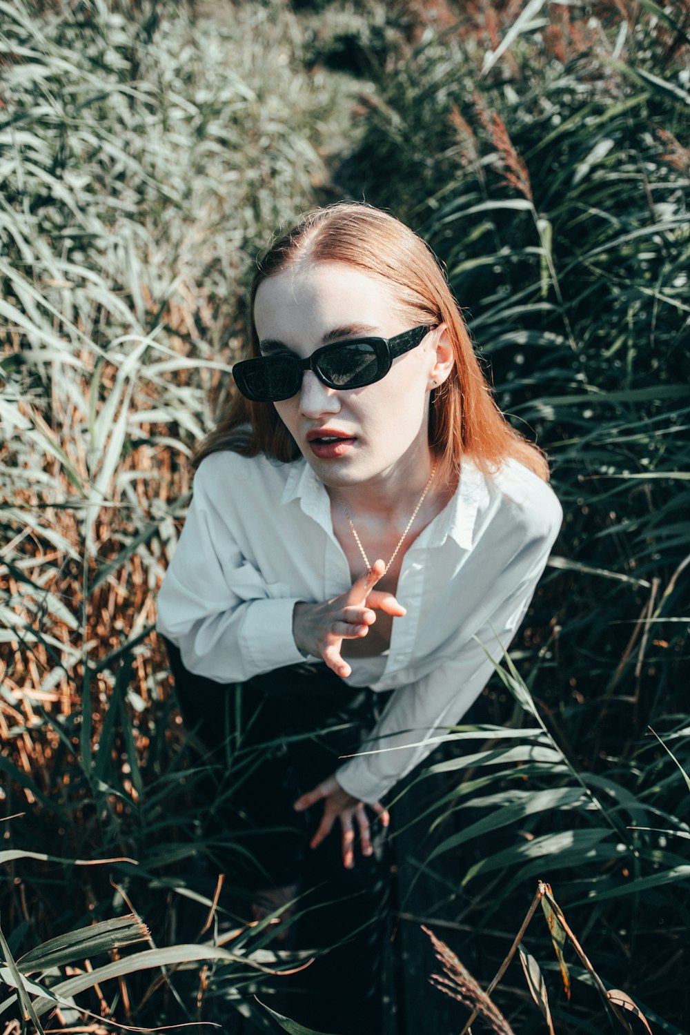 a woman with red hair and black sunglasses in a field of tall grass