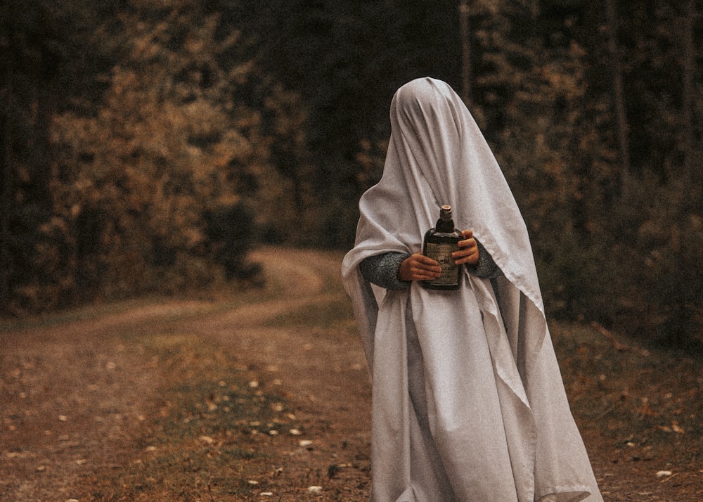 a woman in a white cloak holding a bottle