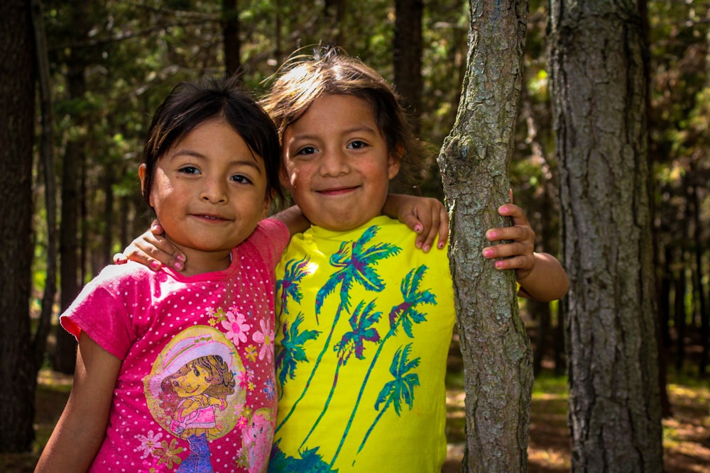 two little girls standing next to each other in the woods